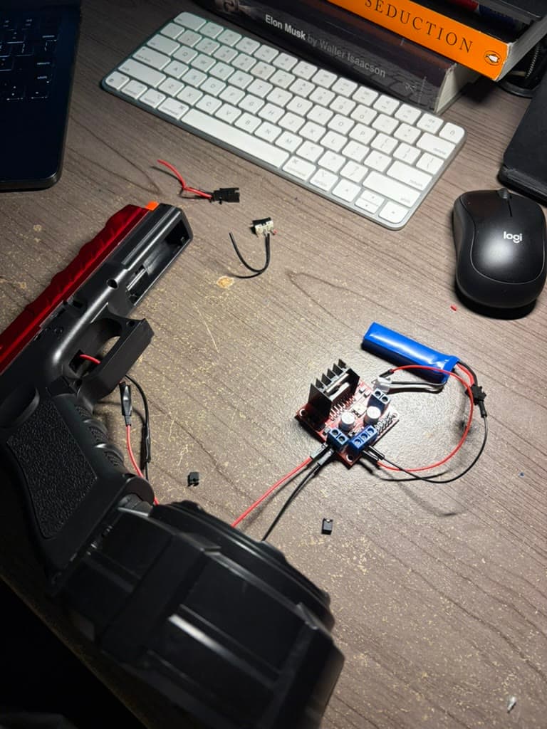 The gel blaster, battery, and L298N motor driver laid out on the workbench.