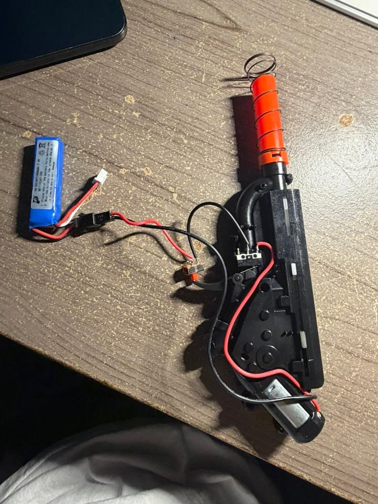 The opened gel blaster showing its battery, wiring, motor, and firing mechanism.